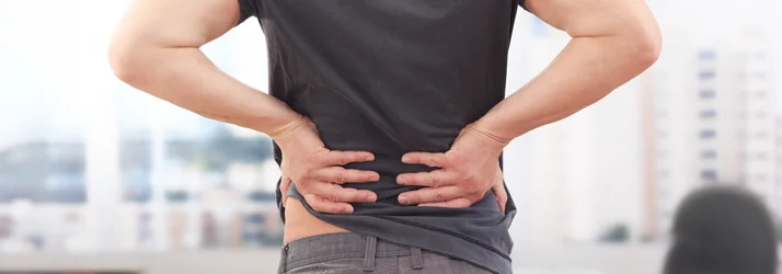 A person standing and holding their lower back in pain